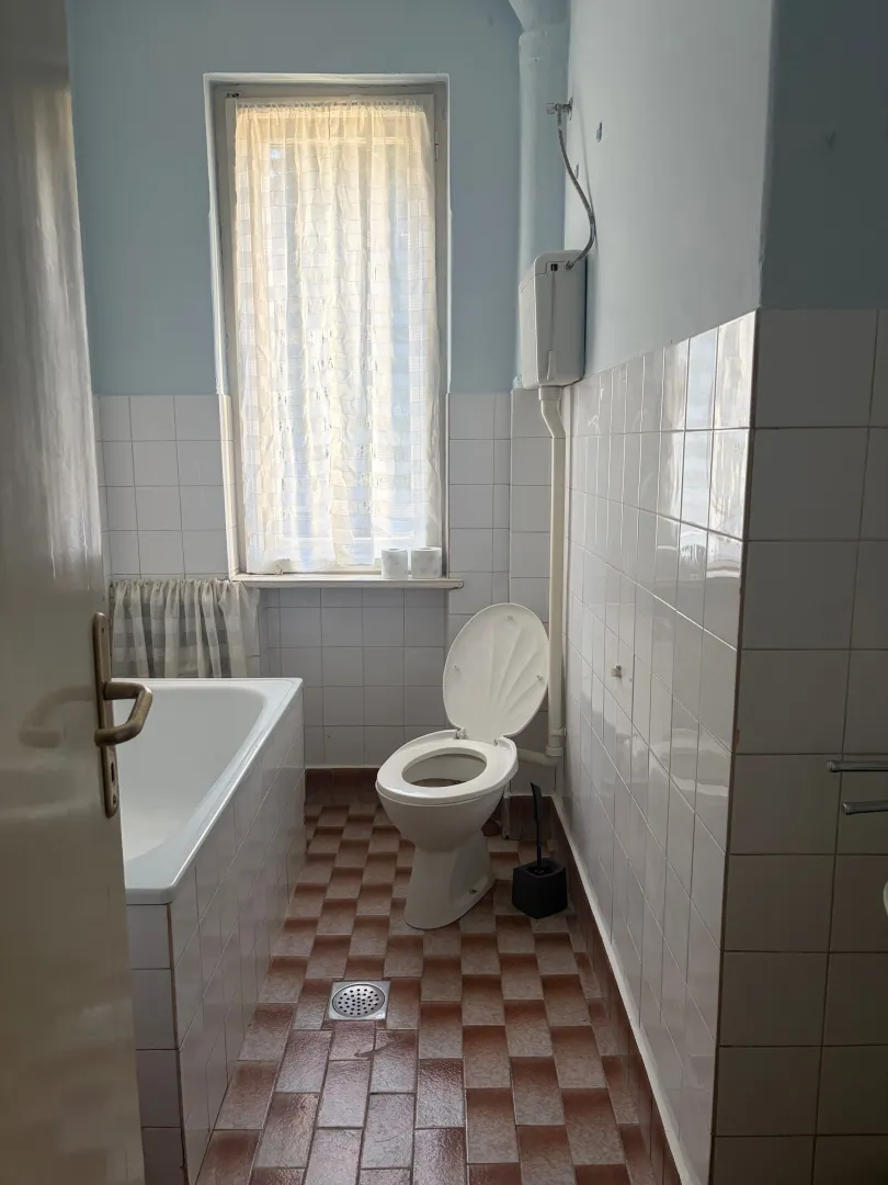 Manje kupatilo sa kadom, toaletom i prozorom.