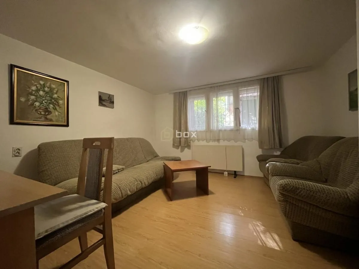 Dnevna soba sa garniturom za sedenje, stočićem i prozorom sa zavesama.