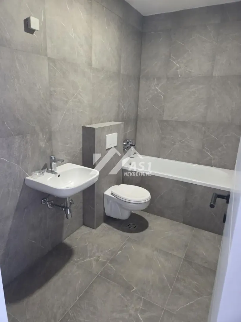 Modern bathroom lined with grey tiles featuring a bathtub, washbasin, and toilet.