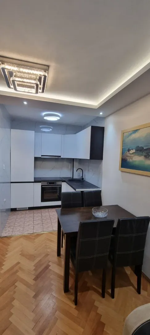 Trpezarijski sto sa stolicama ispred moderne kuhinje sa bijelim elementima.