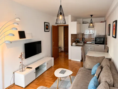 Living room with a sofa, TV, and kitchen in the background. - image 3