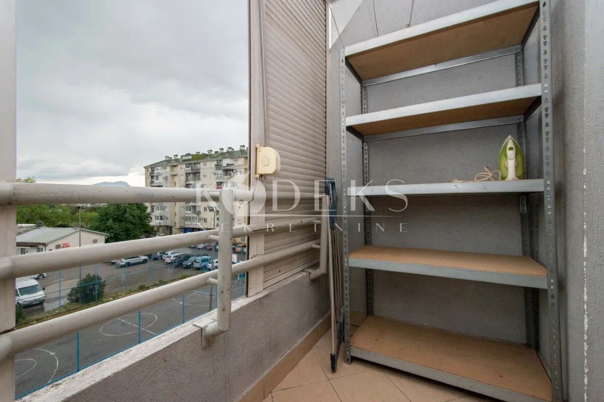 Small covered balcony with a metal shelving unit and a view of the neighborhood.