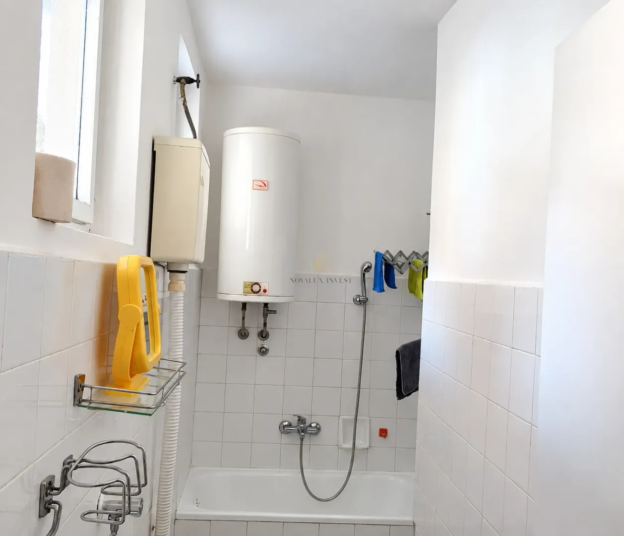 Bathroom with a bathtub, water heater, and white wall tiles.