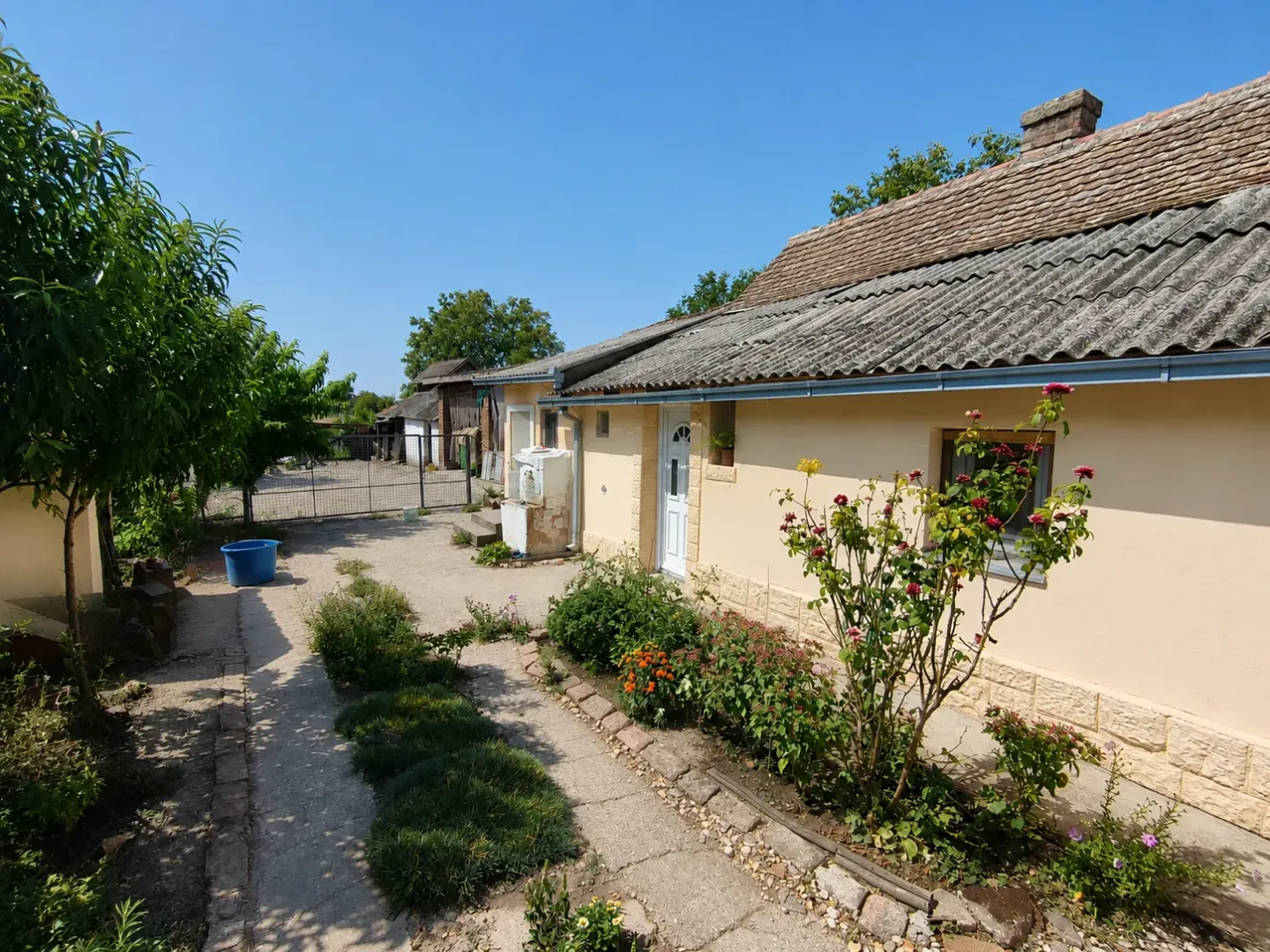 Pogled na dvorište i fasadu kuće sa uređenom stazom i baštom.