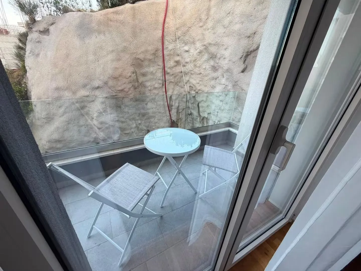 Small balcony with a table and two chairs overlooking a rock face.