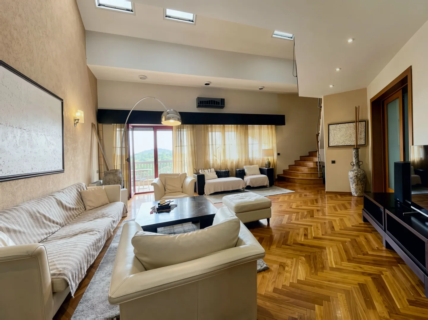 Spacious living room with seating area, wooden flooring, and high ceiling.