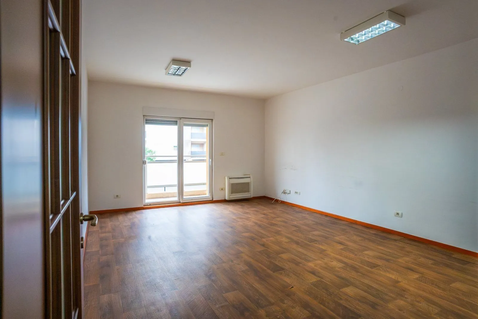 Prazna prostorija sa drvenim podom i izlazom na balkon.