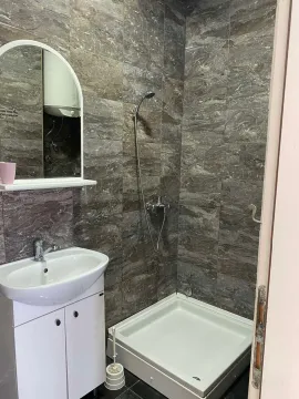 Small bathroom with a shower cabin, sink, and mirror, tiled with marble-effect ceramic tiles. - image 4