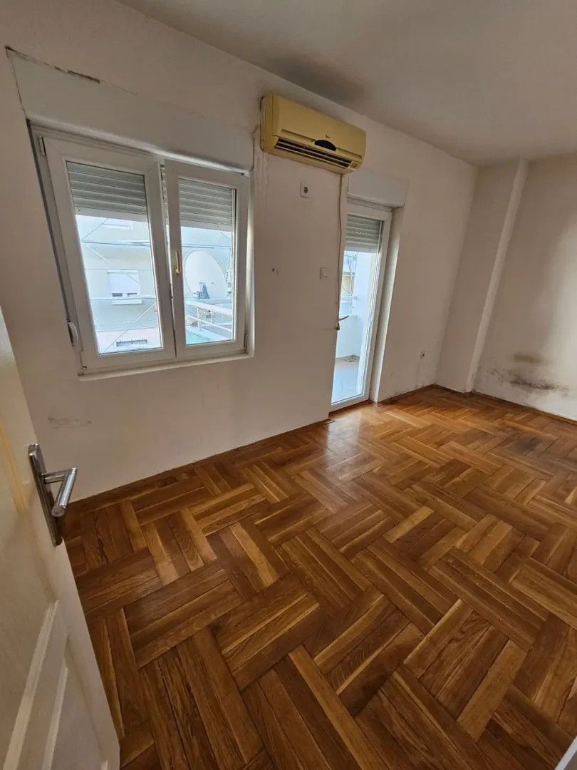 Empty room with wooden parquet flooring, window, and air conditioning unit.