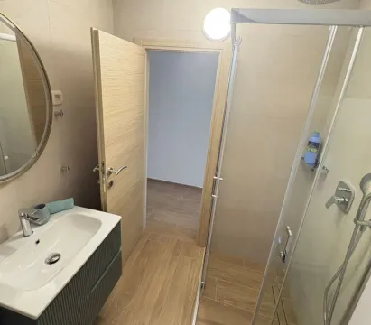 Kupatilo sa umivaonikom, tuš kabinom i otvorenim vratima. - image 7