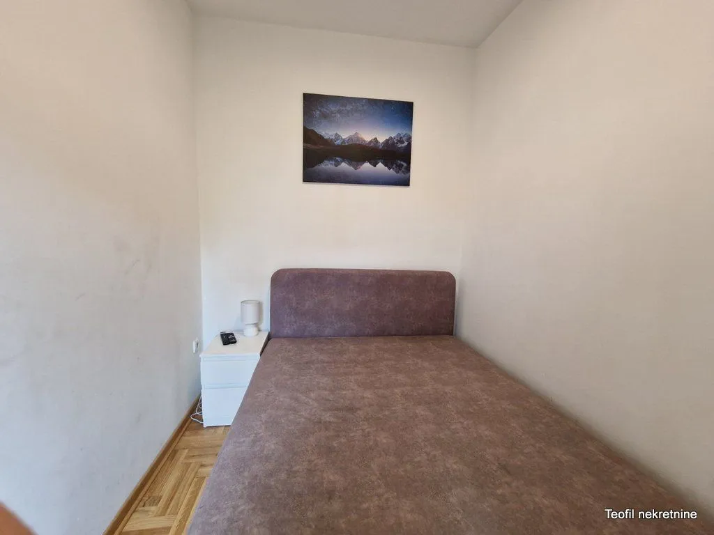 Manja spavaća soba sa bračnim krevetom i noćnim stočićem.