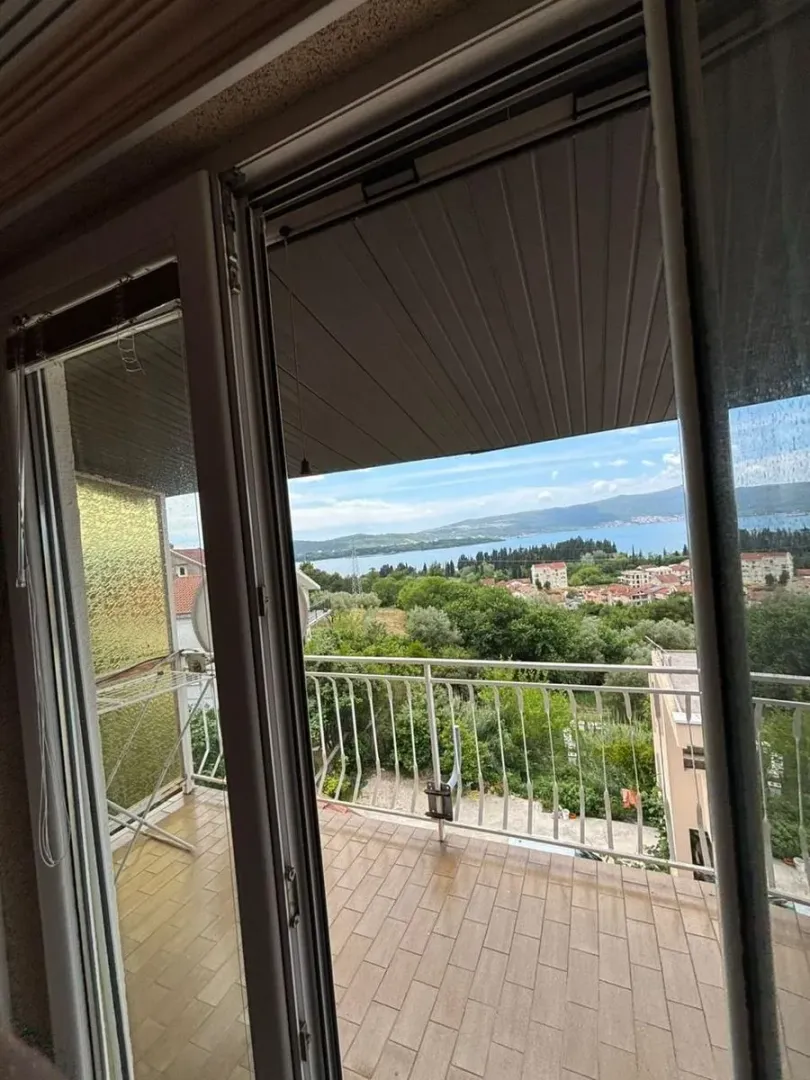 Pogled sa popločane terase na more i okolno naselje kroz balkonska vrata.