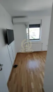 Prazna spavaća soba sa drvenim podom, televizorom na zidu i prozorom. - image 7