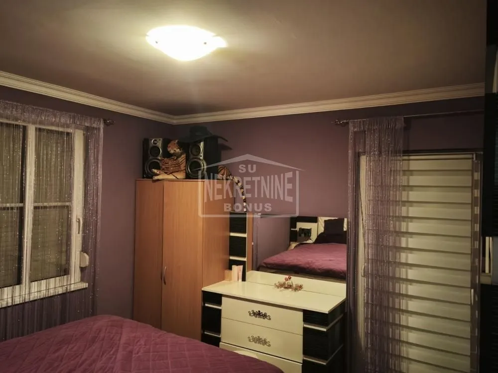 Nameštena spavaća soba sa ljubičastim zidovima i ormanom.