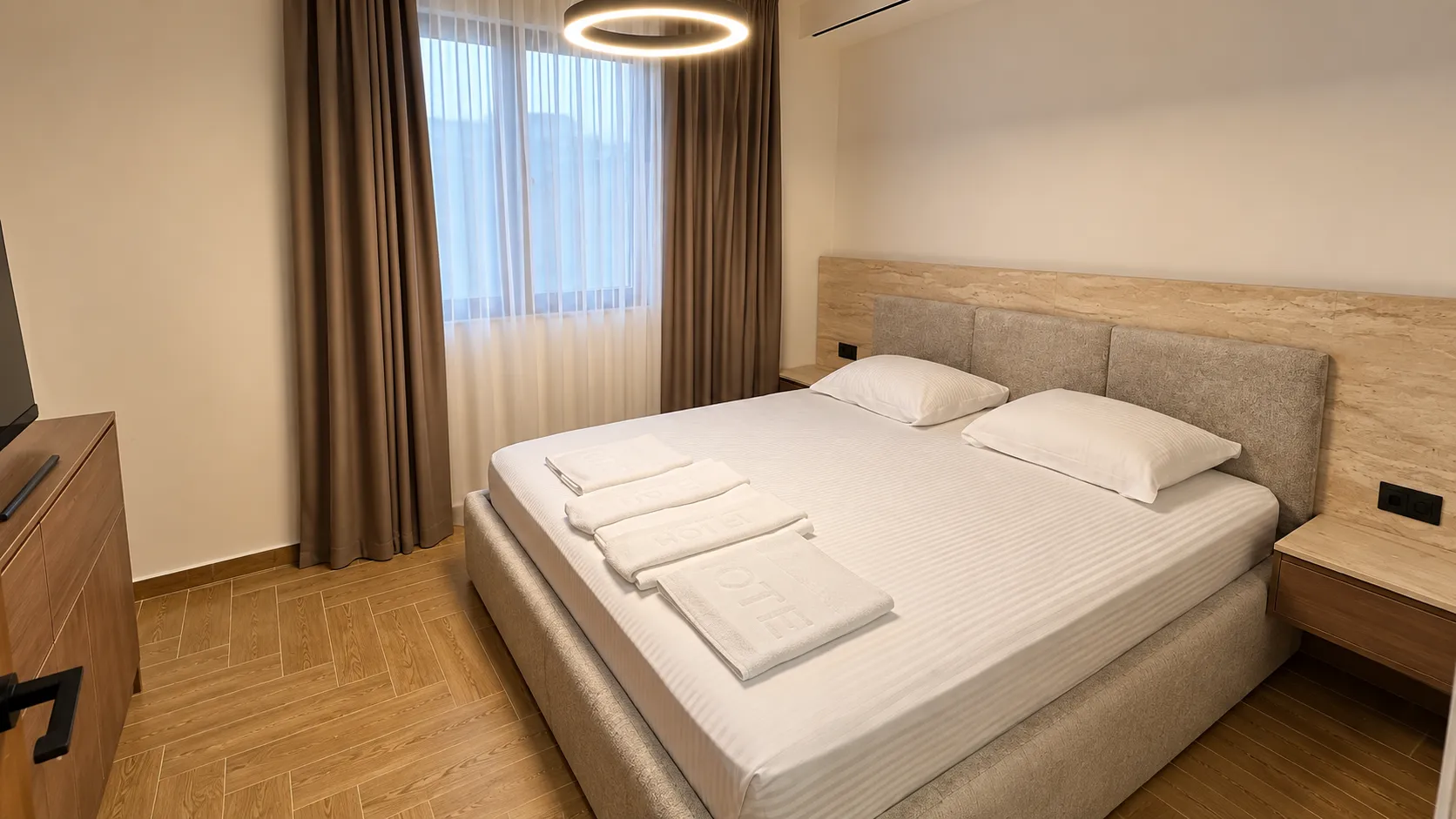 Comfortable bedroom with a double bed, wooden flooring, and a window with curtains.