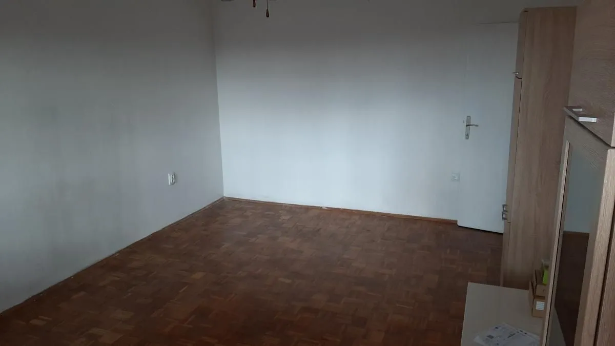 Prazna soba sa parketom i belim zidovima.