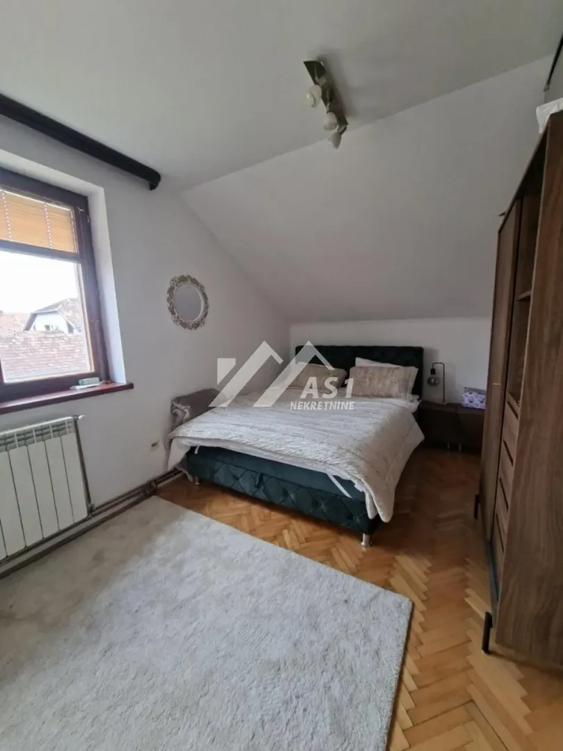 Nameštena spavaća soba sa bračnim krevetom, ormarom i krovnim kosinama.