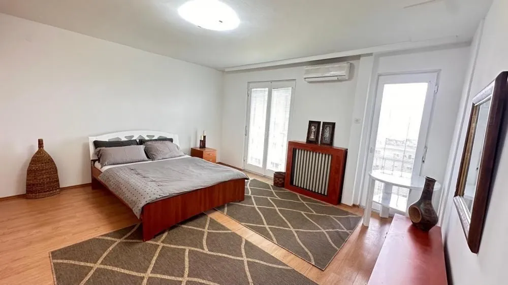 Bedroom with a double bed, wooden flooring, and two terrace doors.