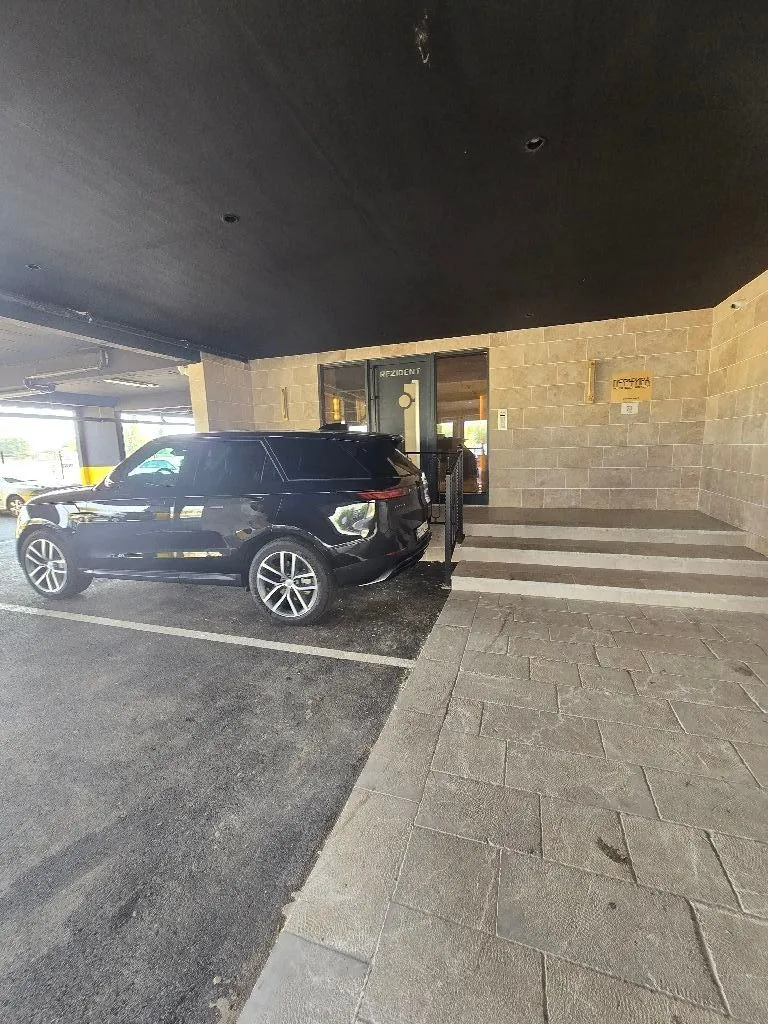 Building entrance with a parking space and a parked SUV.