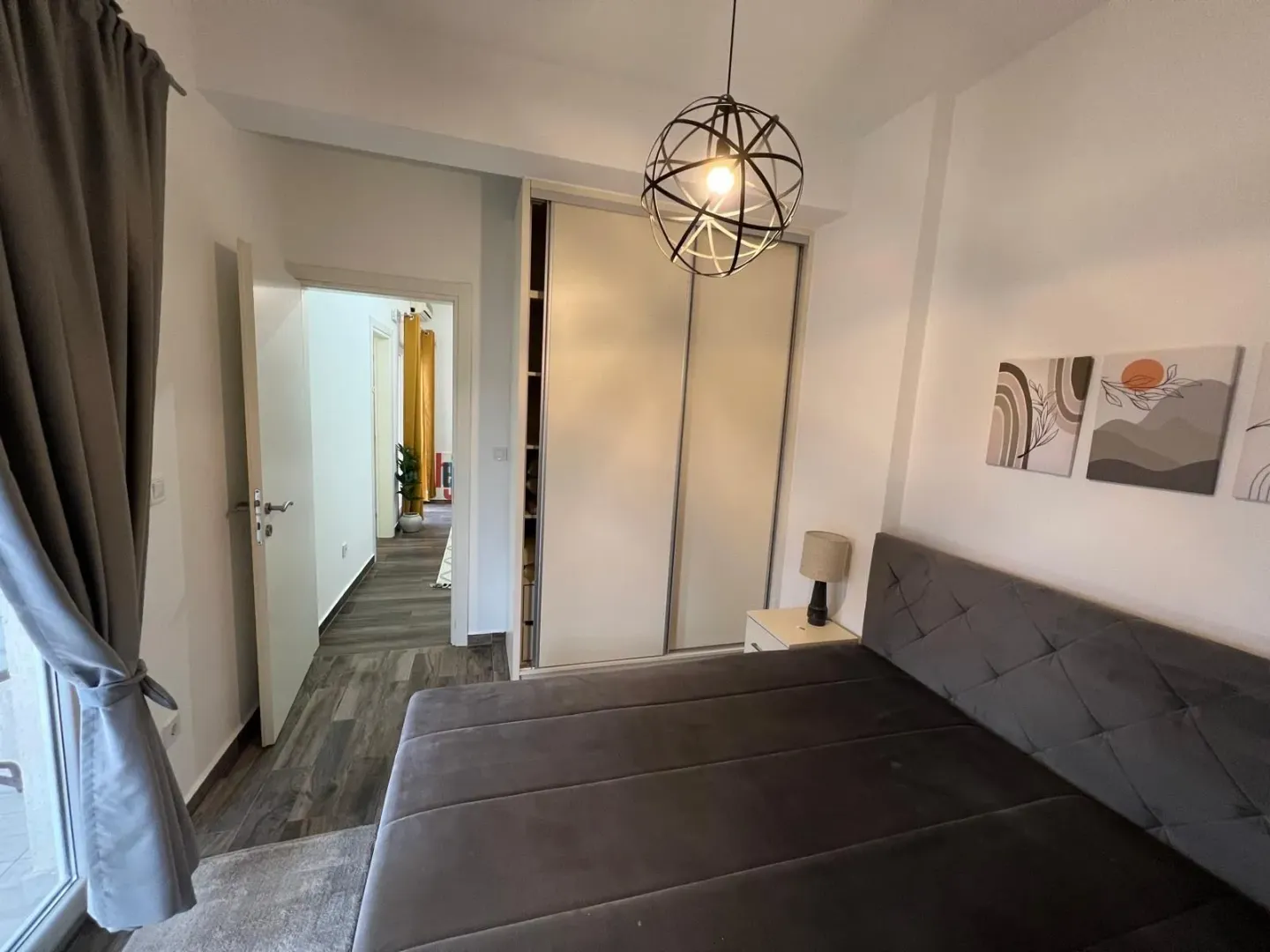 Namještena spavaća soba sa bračnim krevetom, ormarom i modernim lusterom.