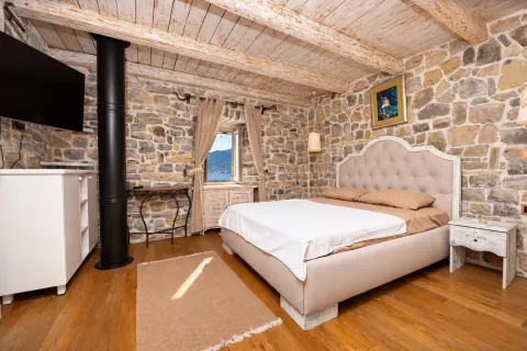 Rustic bedroom with stone walls, wooden ceiling, and a view of the sea through the window. - image 8