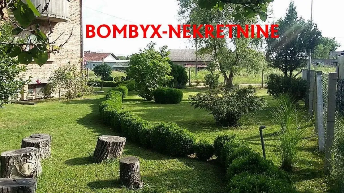 Lepo uređeno dvorište sa travnjakom, drvećem i ukrasnim žbunjem.