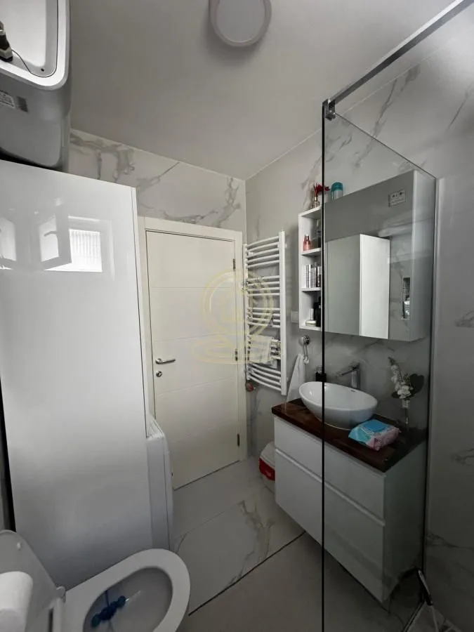Savremeno opremljeno kupatilo sa umivaonikom, tuš kabinom i belim sanitarijama.