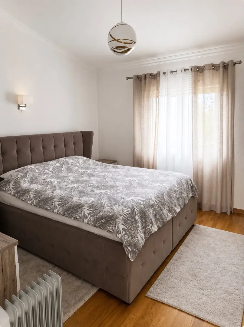 Furnished bedroom with a double bed, window, and curtains.