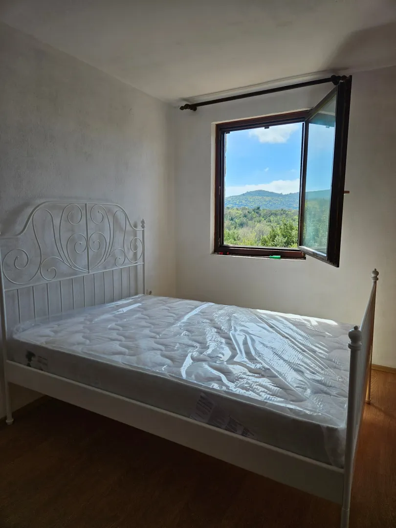 Bedroom with a white metal bed and an open window with a view of nature.