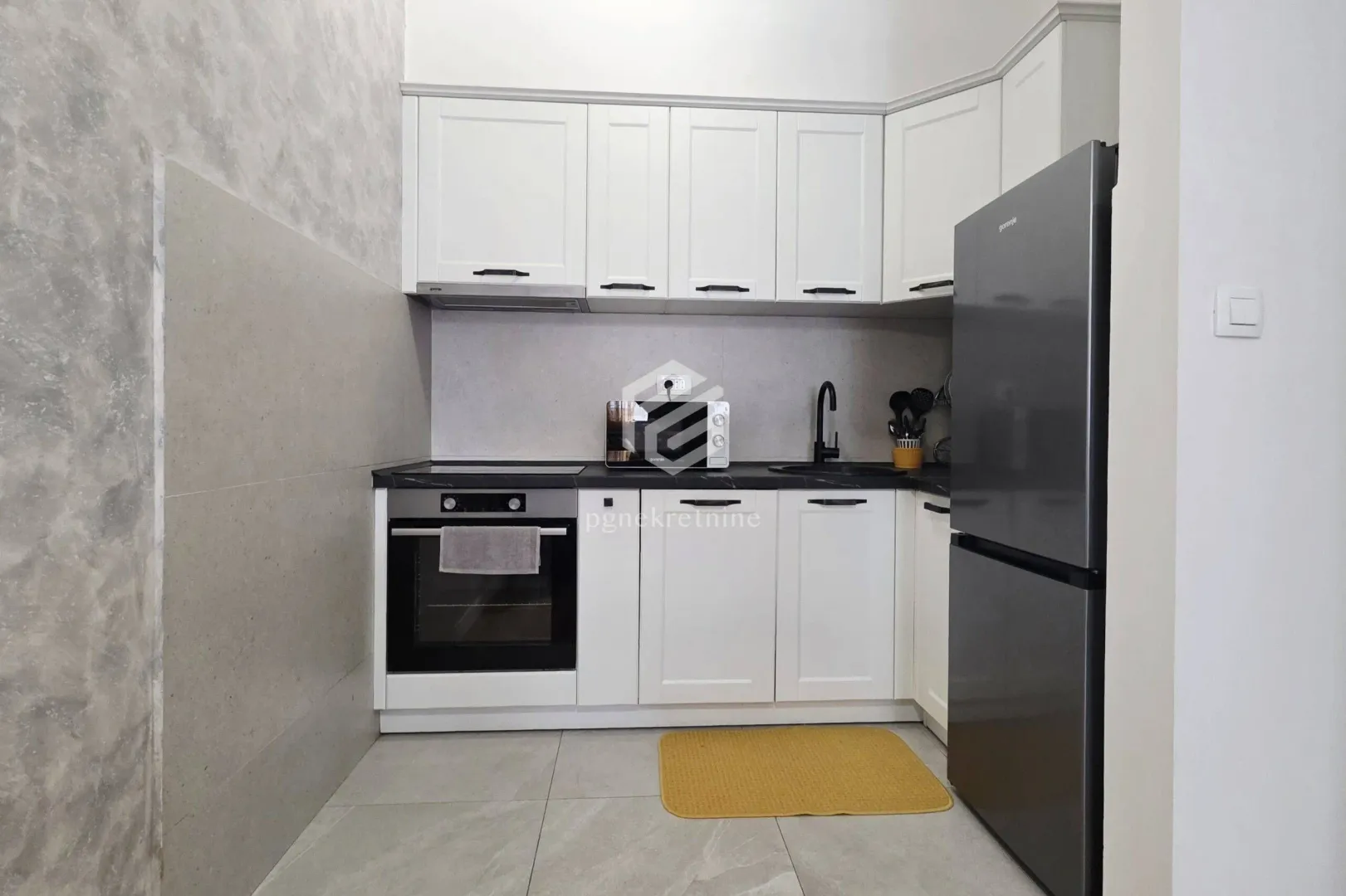 Small kitchen with white cabinets and a dark refrigerator.