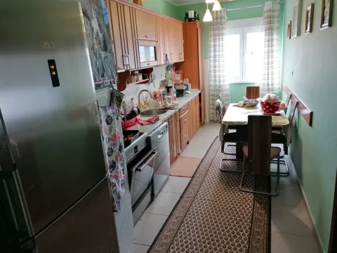 Dugačka kuhinja sa drvenim elementima i trpezarijskim stolom pored prozora. - image 2