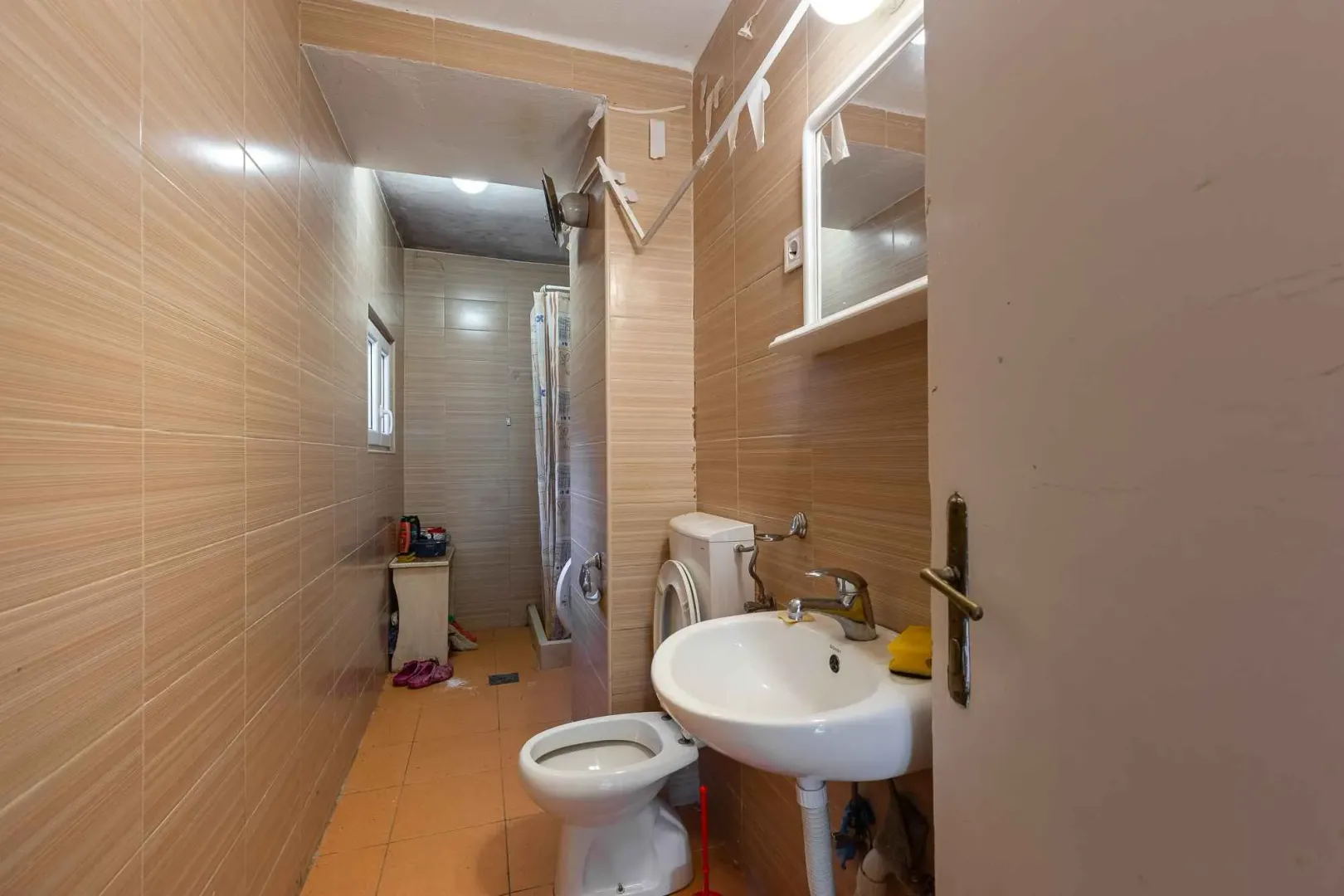 Manje kupatilo obloženo keramičkim pločicama sa umivaonikom i wc šoljom.