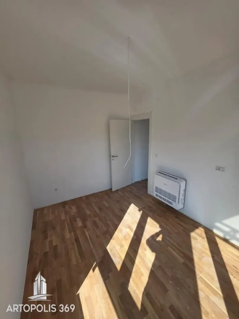 Empty room with wooden flooring, an air conditioning unit, and an open door.