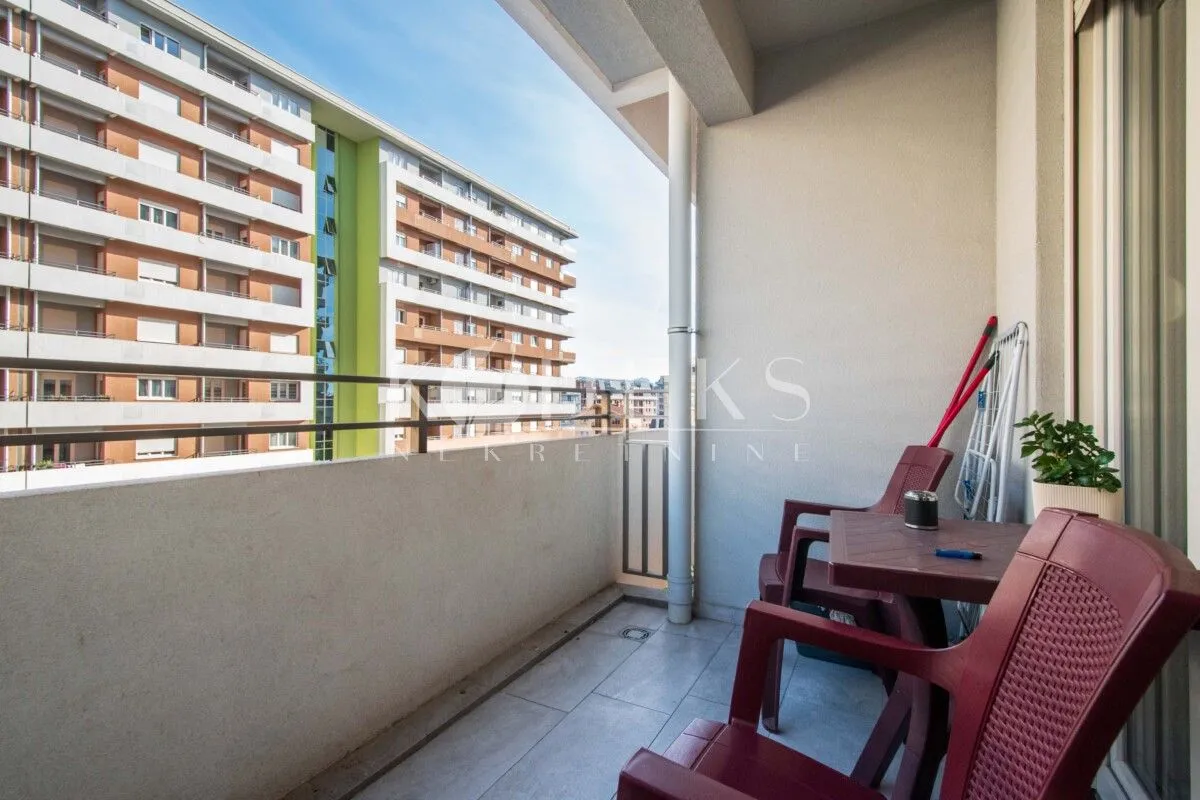 Natkriveni balkon sa garniturom za sjedenje i pogledom na okolne zgrade.