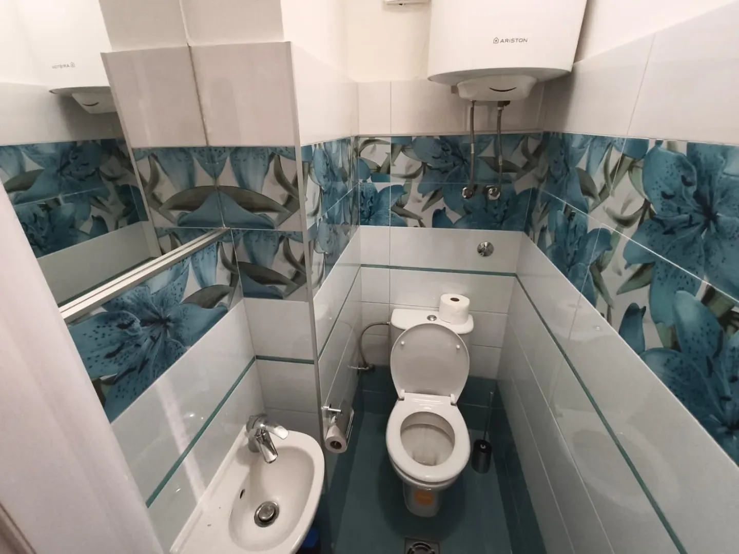 Small bathroom with floral patterned tiles, a sink, and a toilet.