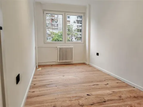 Prazna soba sa drvenim podom i prozorom koji gleda na zgrade. - image 6