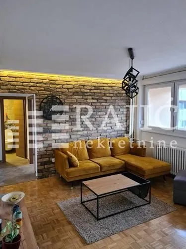 Living room with a sectional sofa, brick accent wall, and wooden flooring.
