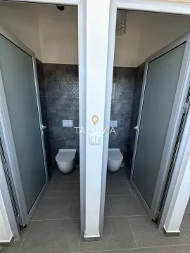 View of two separate toilets with dark tiles and glass doors. - image 7