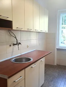 Jednostavna kuhinja sa svijetlim elementima, drvenom radnom pločom i prozorom. - image 2