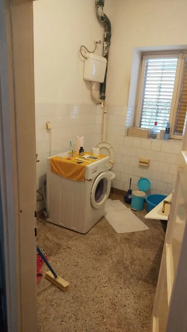 An older bathroom with a washing machine and window in need of renovation.
