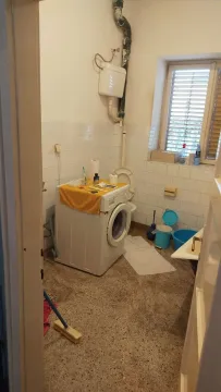 An older bathroom with a washing machine and window in need of renovation. - image 4