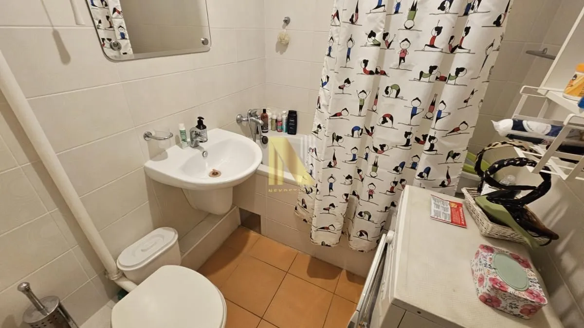 Kupatilo opremljeno umivaonikom, WC šoljom i kadom sa zavesom.
