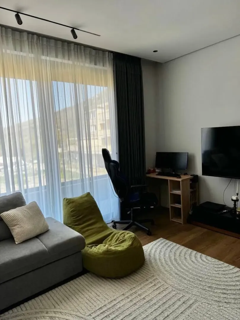 Dnevni boravak sa garniturom, TV-om i radnim stolom pored prozora.