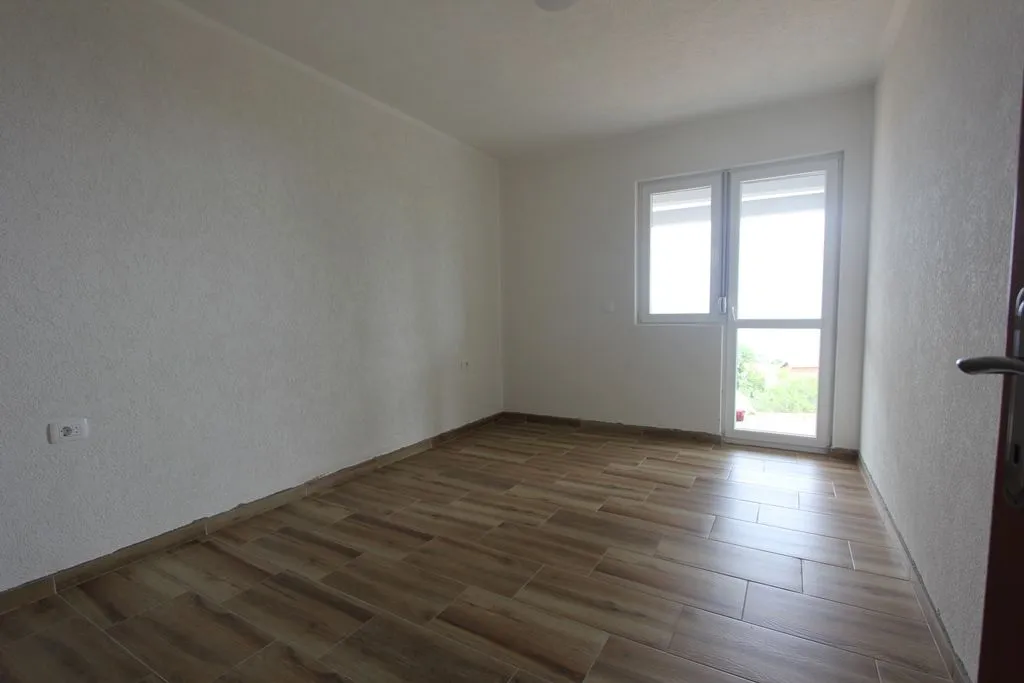 An empty room with light walls and wood-pattern tiled flooring.