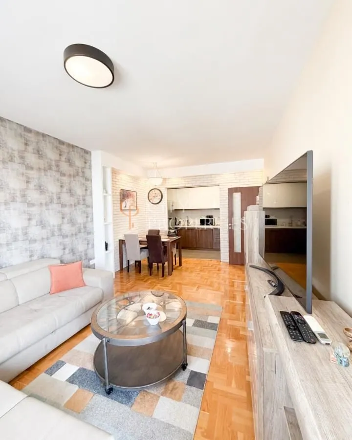 Living room with sofa, television, and dining area in the background.
