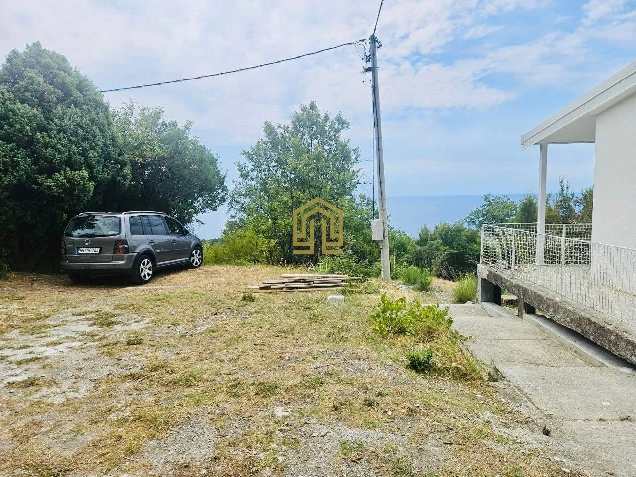 Eksterijer kuće sa dvorištem, parkiranim automobilom i pogledom na prirodu.
