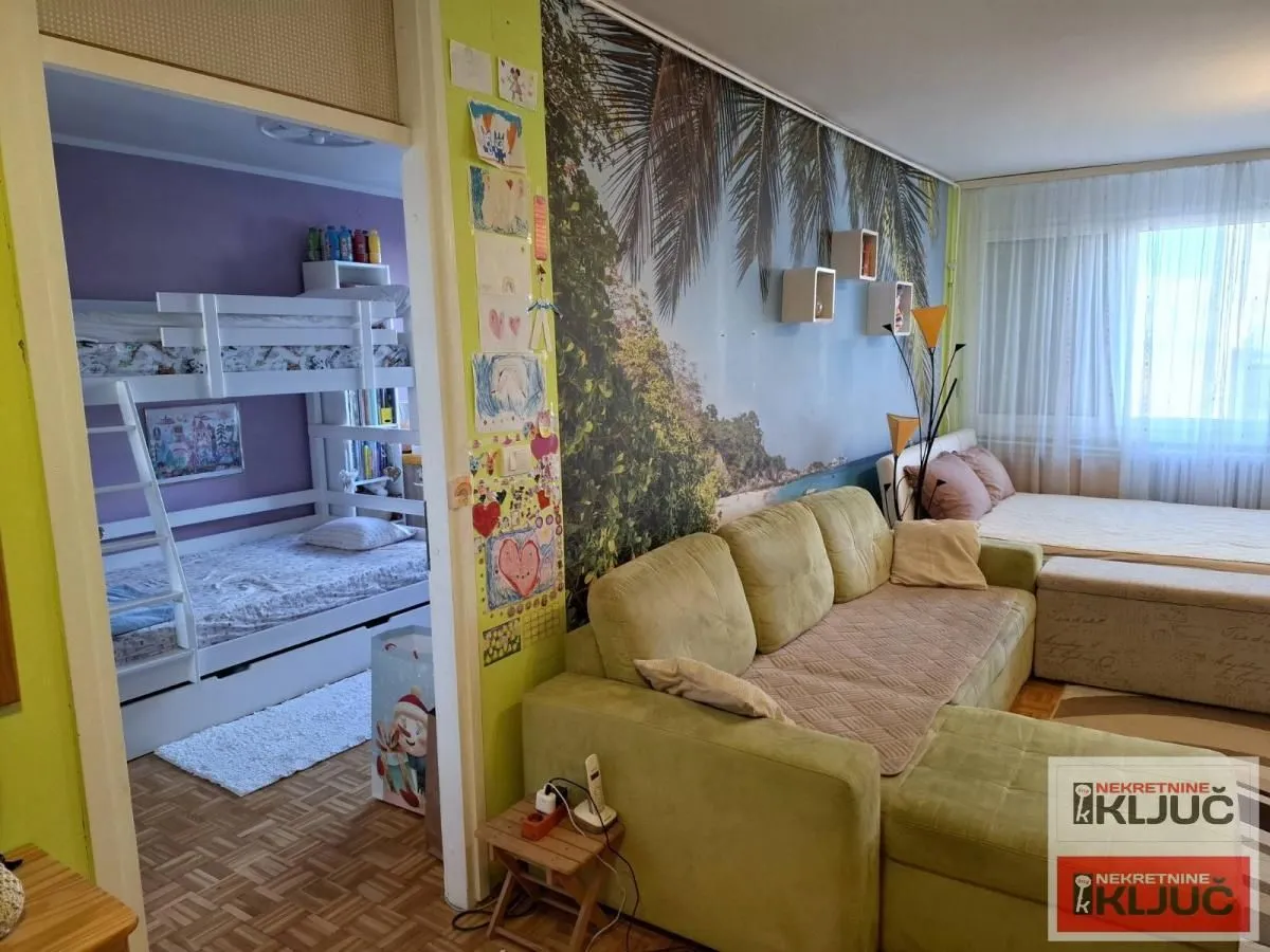 Dnevna soba sa garniturom i pogledom na spavaću sobu sa krevetom na sprat.