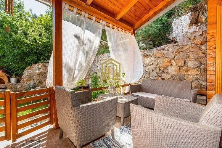 Covered terrace with seating furniture and a view of greenery.