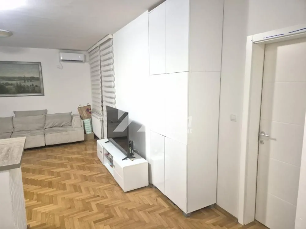 Pogled na dnevnu sobu sa garniturom, televizorom i parketom na podu.
