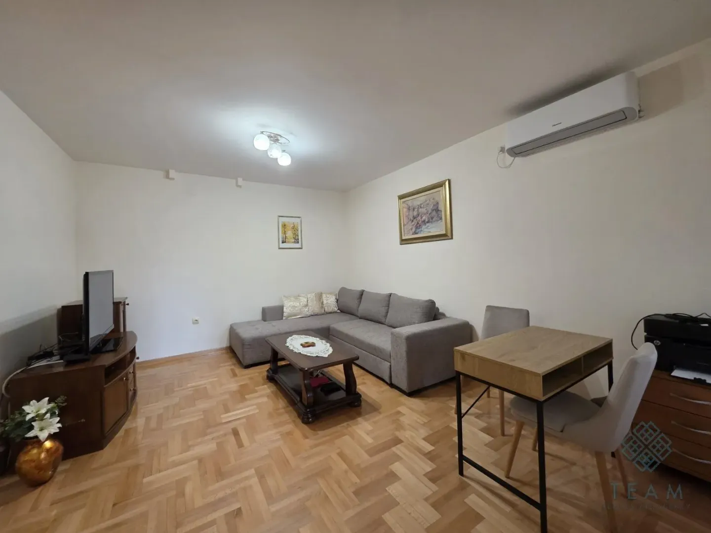 Living room with a sectional sofa, TV, dining table and air conditioning.